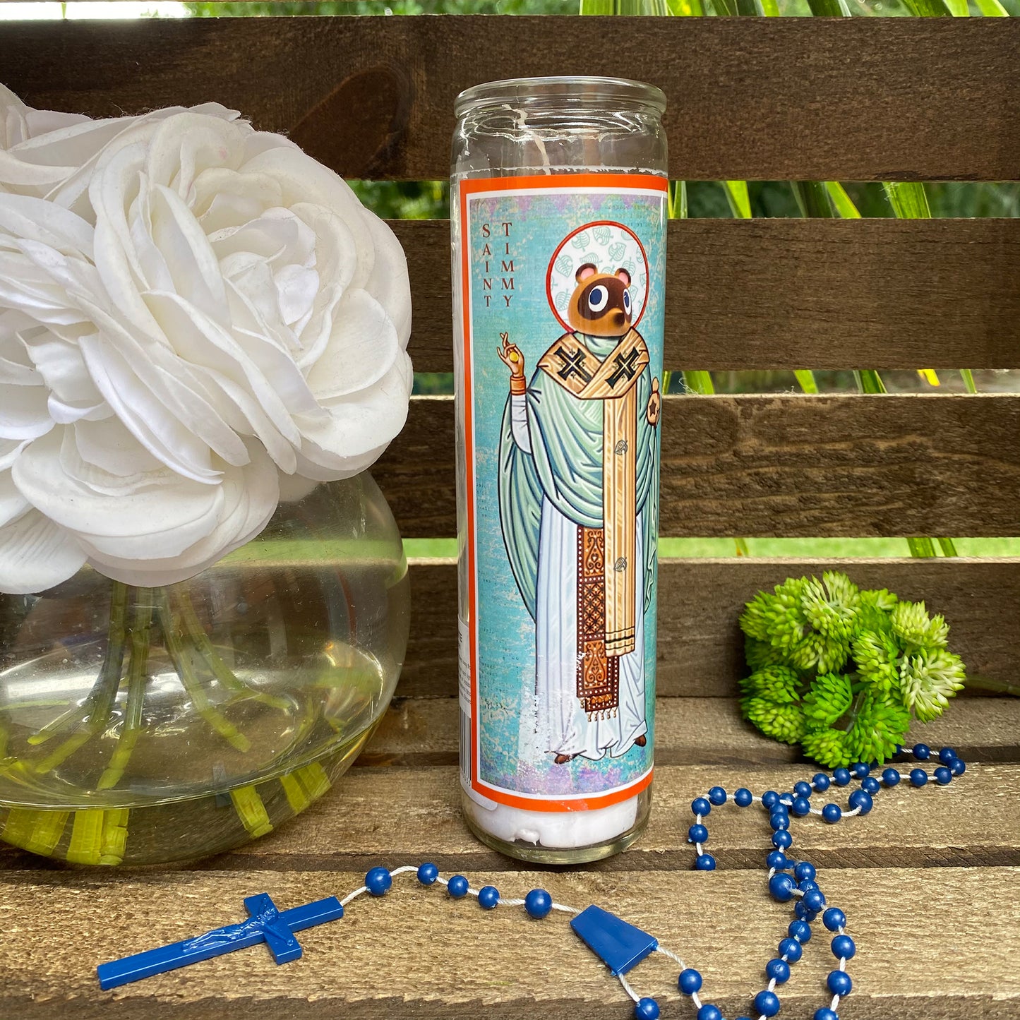 a rosary, a vase with flowers, and a candle on a bench