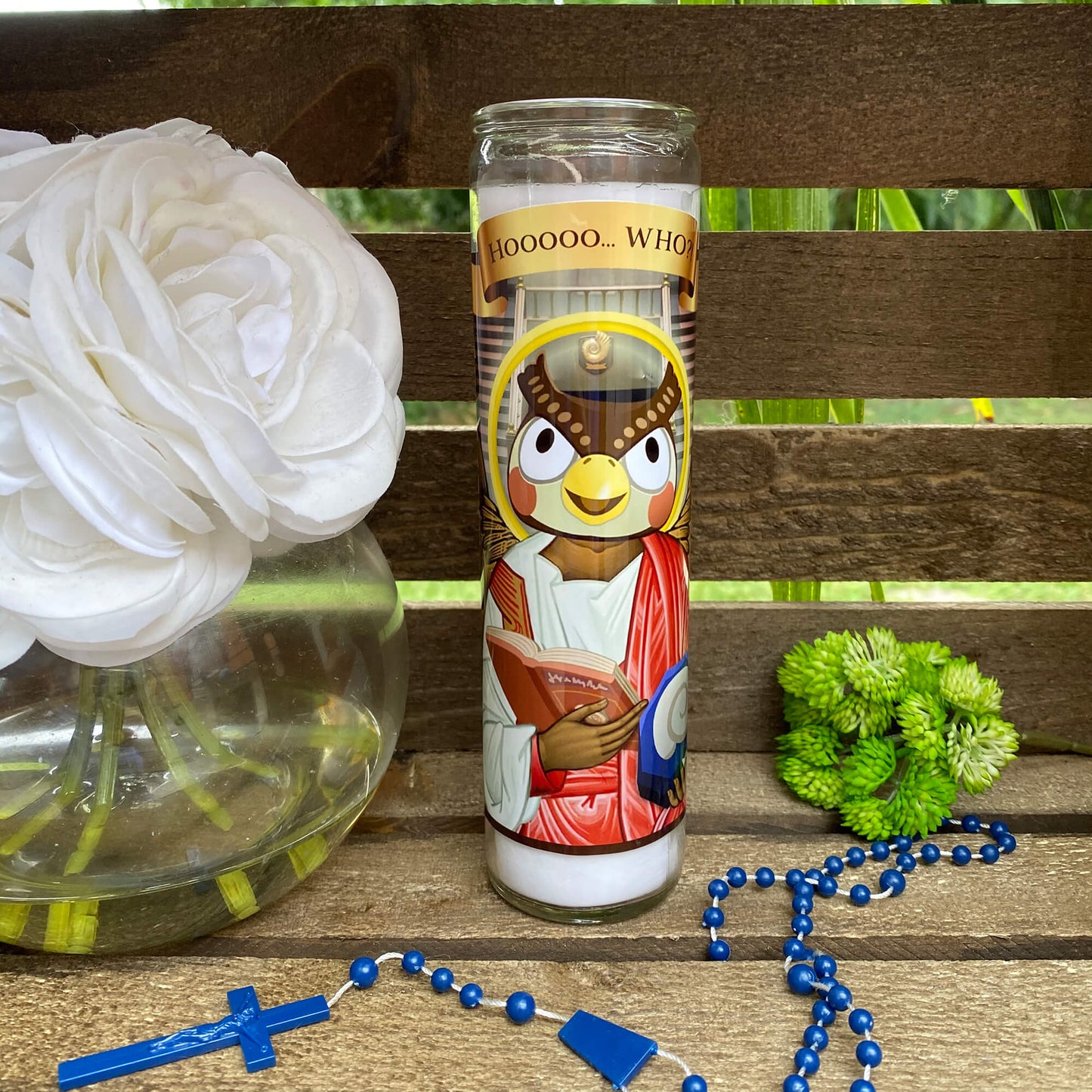 a glass with a picture of a bird on it next to a rosary